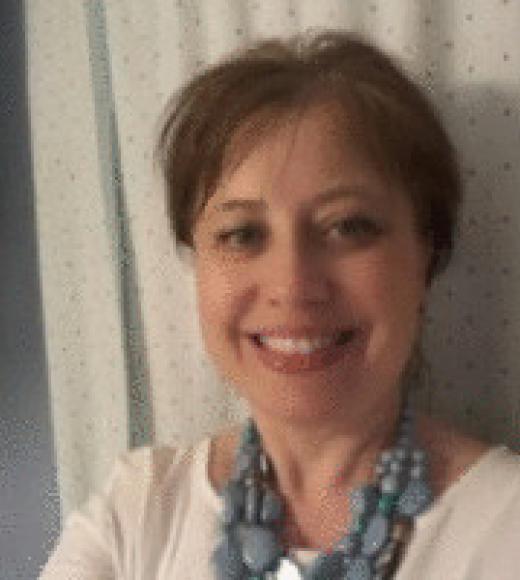 A headshot of Marta Gmurczyk standing in front of a white curtain with small blue dots, wearing a white shirt and a chunky light blue necklace. Marta is smiling big, with brown eyes, short light brown hair, and light-toned skin.