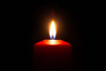 A picture with black background and a red candle. The bottom of the candle fades into black and the candle is lit.