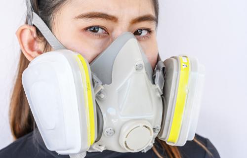A person wearing a half-face grey respirator mask with a white filter on each side.