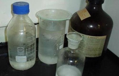 A cluster of unlabeled capped containers and beakers with watch glasses over them. Inside, there is a clear liquid with a white solid.