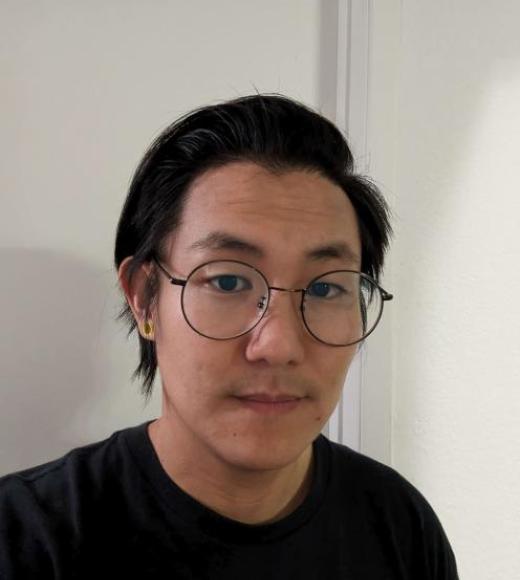 A headshot of Kevin Koshiro standing against a white background wearing a black shirt. Kevin is not smiling, has dark brown eyes, short black hair, round glasses, and light-toned skin.